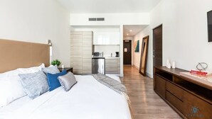 A modern bedroom with a large bed, a small kitchenette, and a wooden dresser.