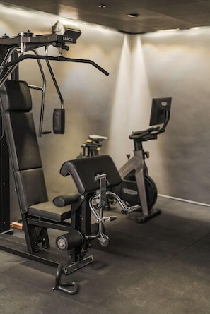 Ein Fitnessraum mit Kraftgeräten, einer Bank und einem Ergometer.