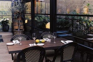Un área de comedor al aire libre con una mesa de madera preparada para dos personas, rodeada de sillas de mimbre.