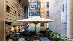Un espace extérieur aménagé avec des tables et des chaises, un grand parasol et un mur portant une inscription.