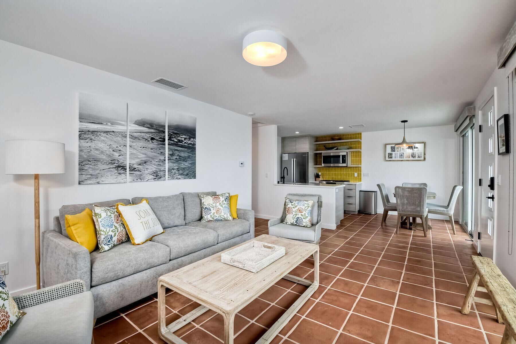 A modern living room with a grey sofa, a coffee table, and a dining area with wicker chairs.