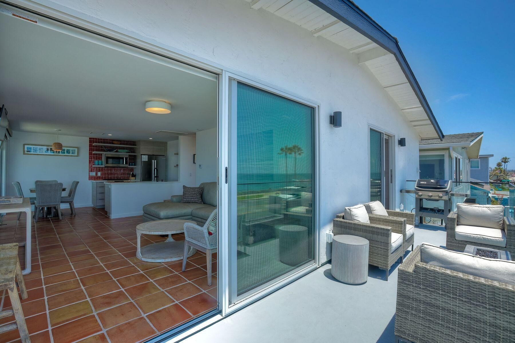 Un espace de vie moderne comprenant un coin repas, une cuisine et un balcon aménagé avec du mobilier d’extérieur.
