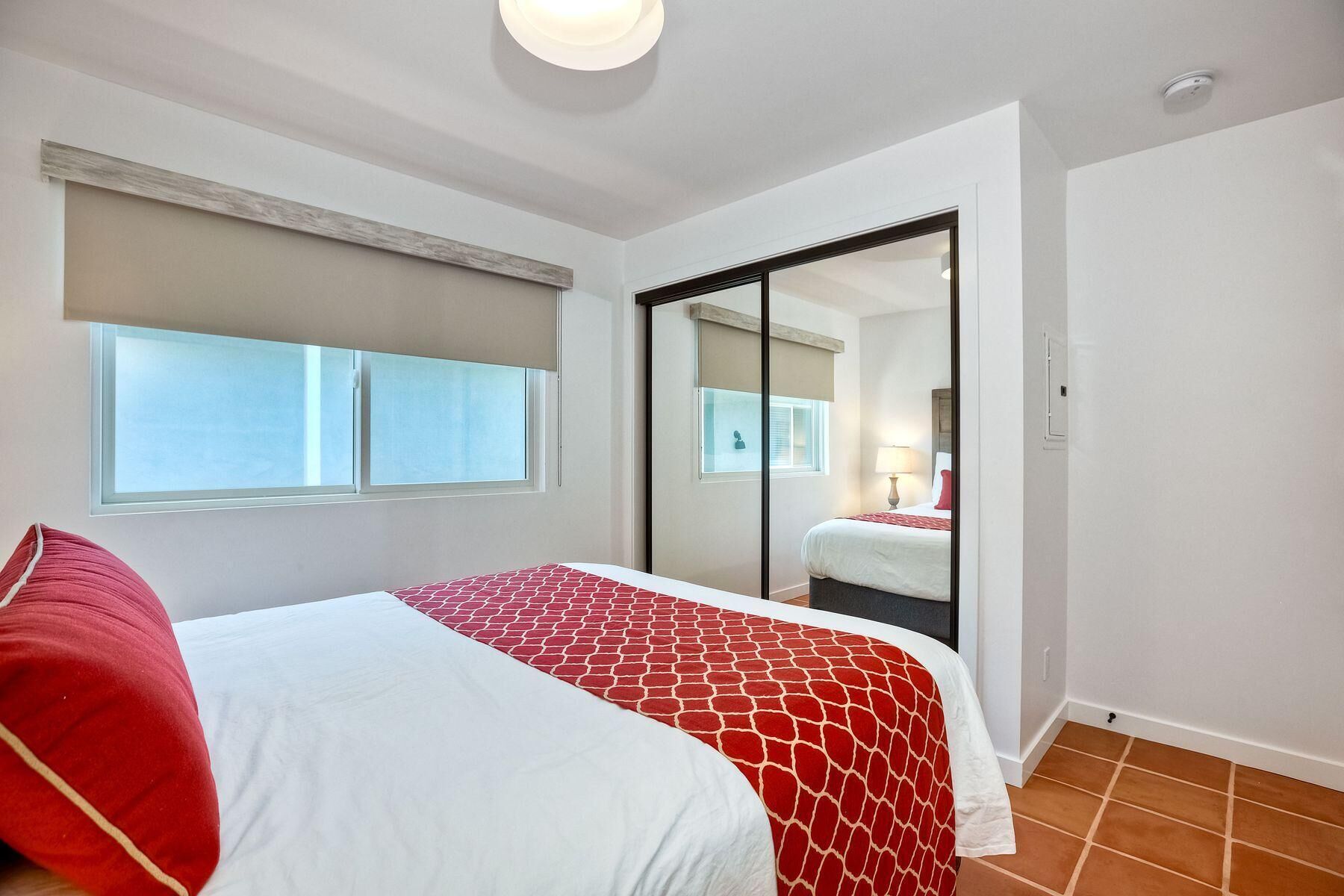 A bedroom with a bed, a window, a sliding door, and a tiled floor.