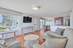 Uma sala de estar moderna com sofá, cadeiras, uma mesinha e uma cozinha com micro-ondas e geladeira.