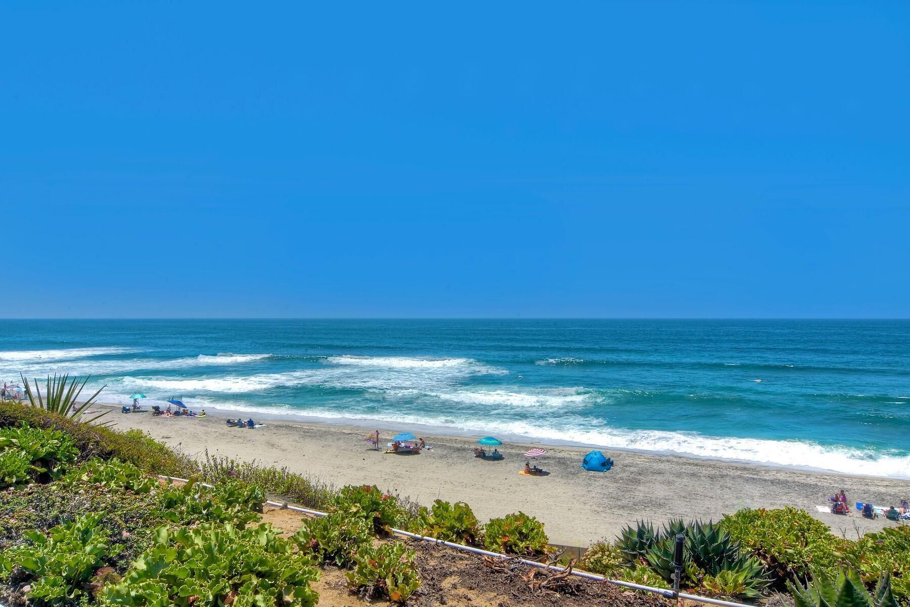 A beach with waves, umbrellas, and people.