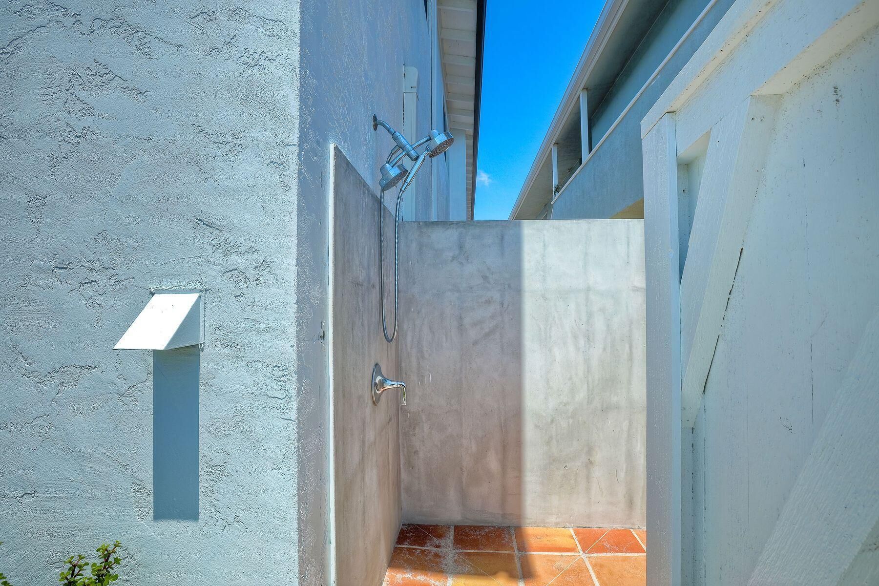 Un étroit couloir extérieur, avec un mur en béton et un sol carrelé, qui mène à une porte.