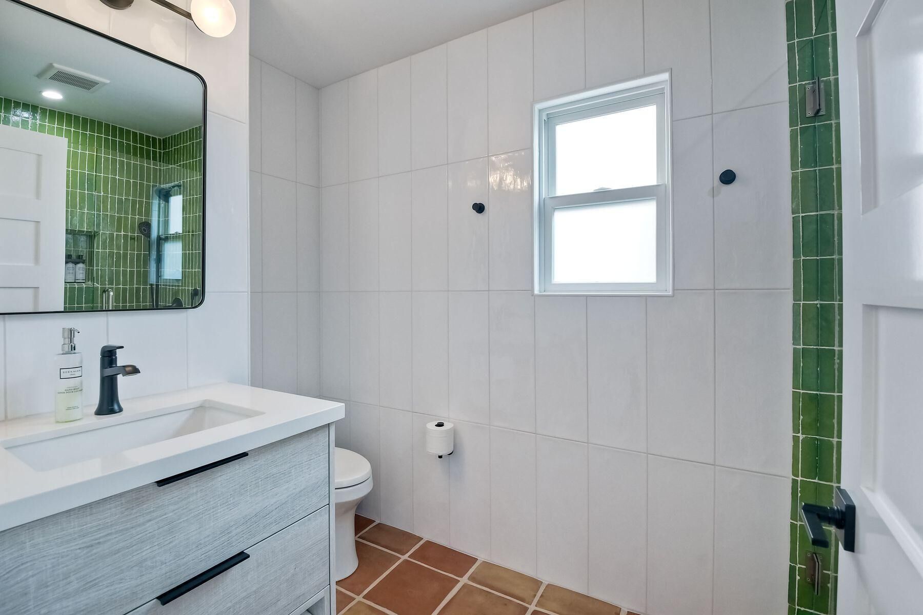 A bathroom with a white sink, a mirror, a toilet, and a window.