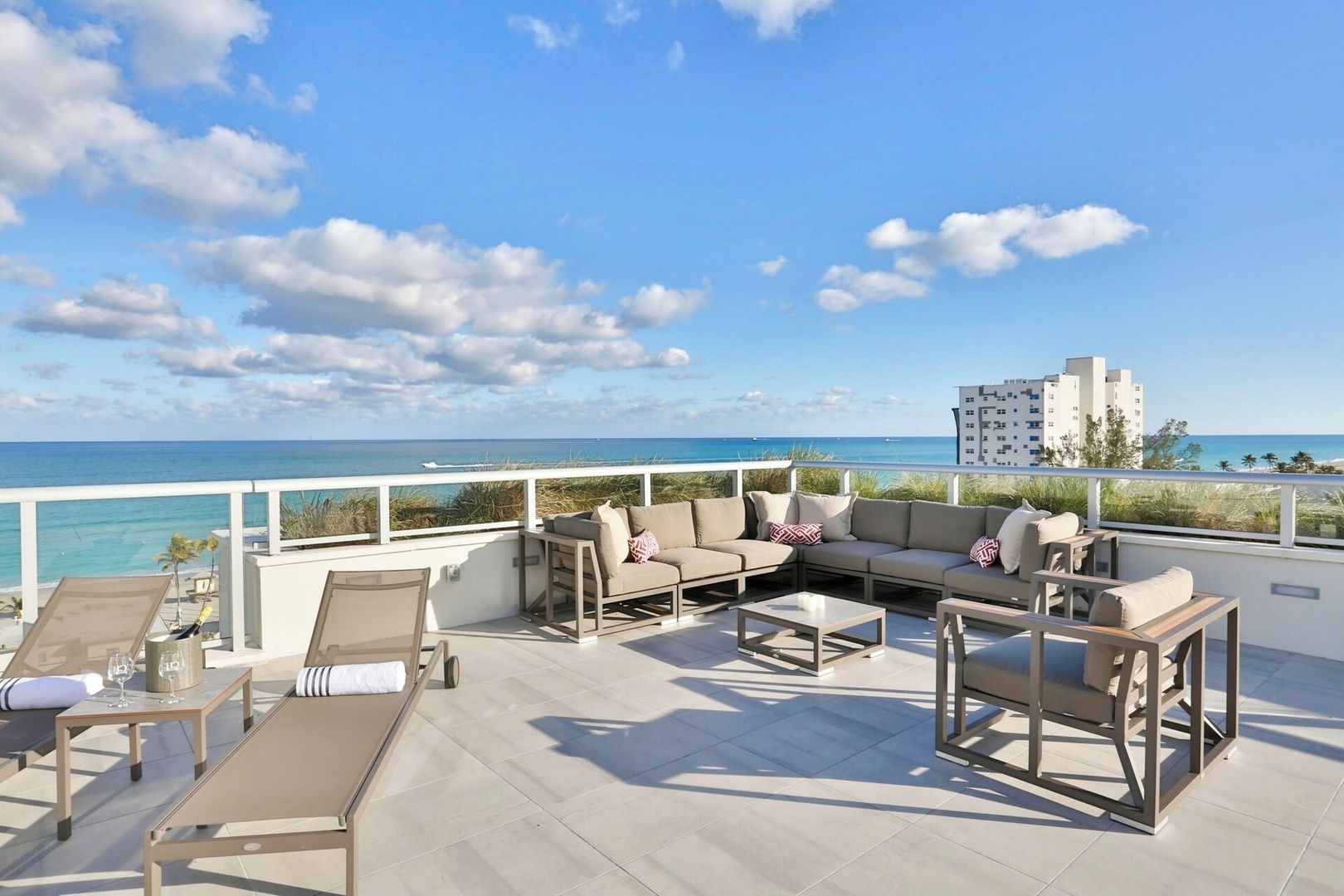 Eine Dachterrasse mit Blick auf das Meer, möbliert mit Sofas und Tischen, mit einem Gebäude im Hintergrund.