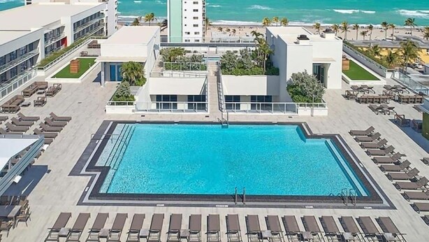En pool på taket med utsikt över havet, omgiven av solstolar och en byggnad med modern design.