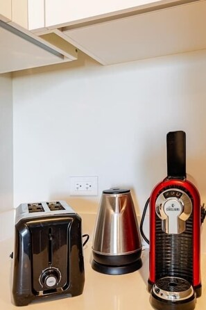 Un plan de travail de cuisine avec un grille-pain noir, une bouilloire électrique argentée et une machine à expresso rouge.