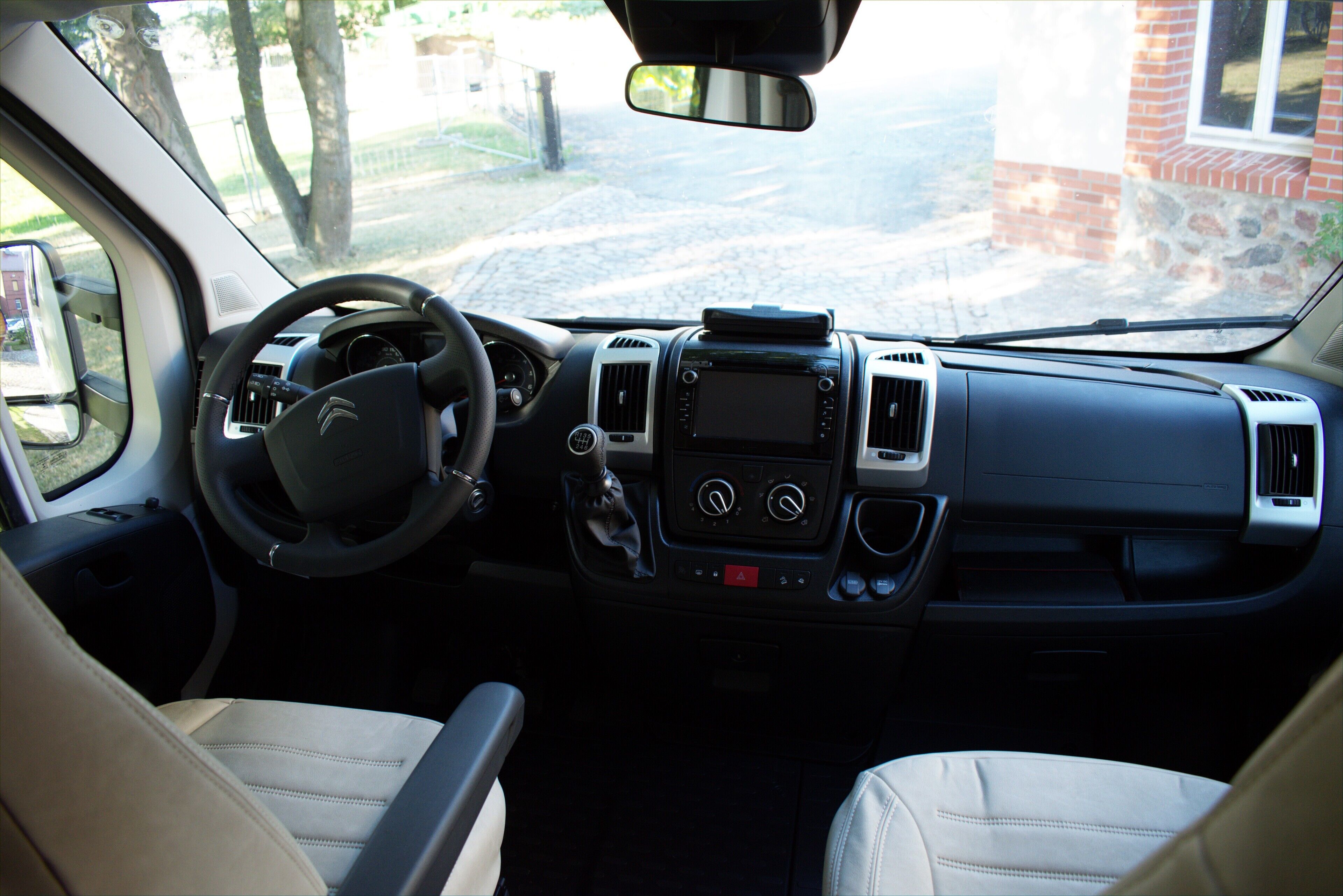 The interior of a vehicle with a steering wheel, dashboard, and two beige seats.