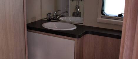 A compact bathroom with a sink, mirror, and toilet.