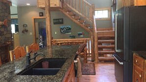 A kitchen with granite countertops, a black refrigerator, wooden cabinets, a stone accent wall, a wooden staircase, and a dining area with wooden chairs. - Work Remote in Paradise on North Creek (North Creek)