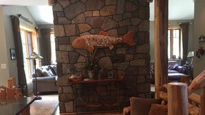 A cozy living room with a stone fireplace, wooden furniture, and a large rug. - Work Remote in Paradise on North Creek (North Creek)