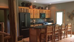 A rustic kitchen with wooden cabinets, a refrigerator, a microwave, and a dining area with wooden chairs. - Work Remote in Paradise on North Creek (North Creek)