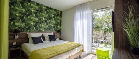 A bedroom with a bed, a nightstand, a lamp, a green chair, and a view of the outdoors.