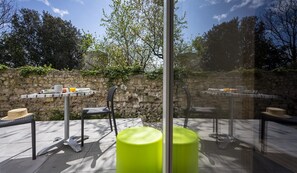 An outdoor patio with tables and chairs, a stone wall, and a glass partition.