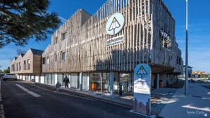 A modern building with a unique wooden facade, labeled 'athome residence'. It features a sign indicating amenities like access, parking, and a local velo.
