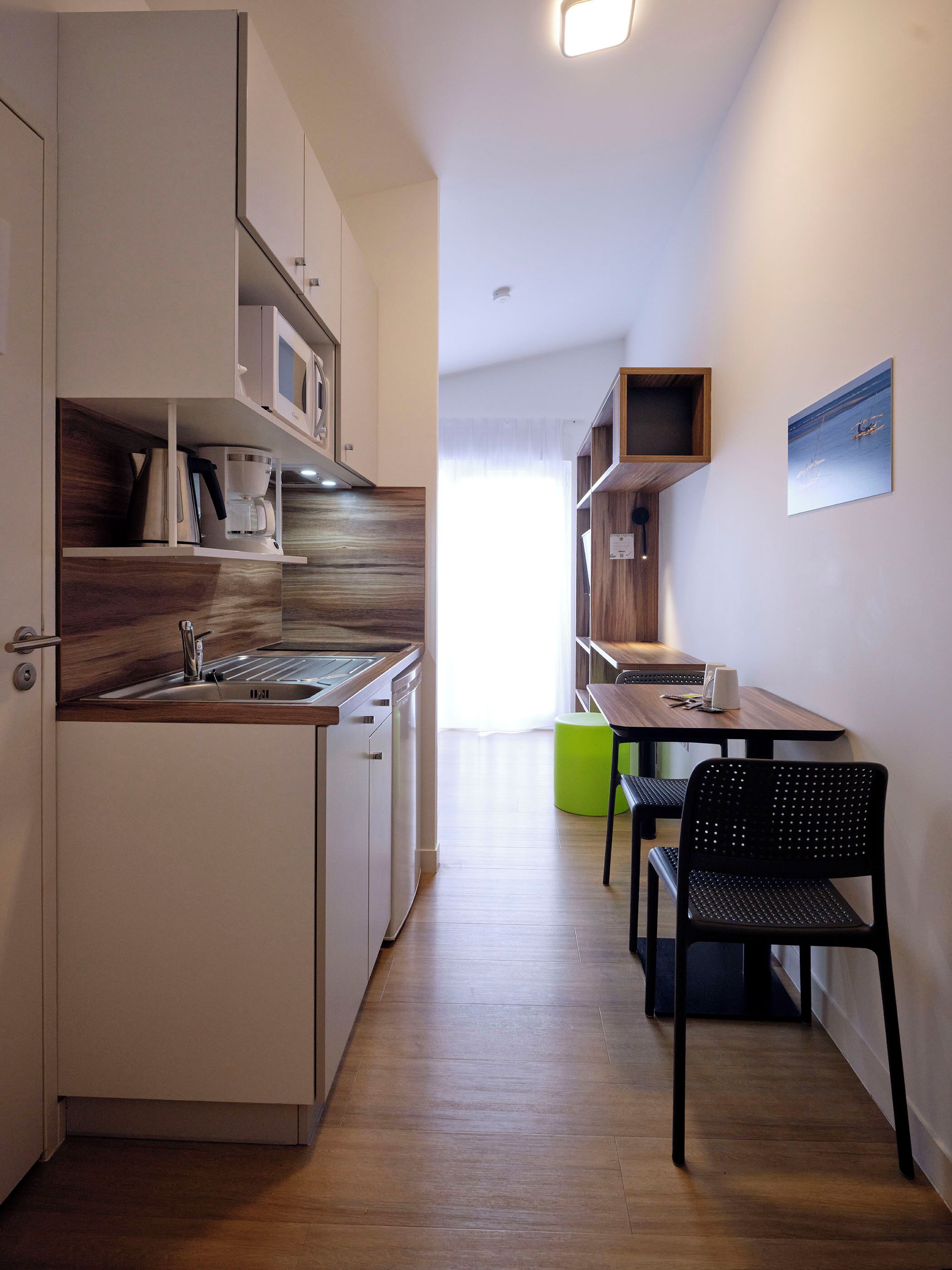 A modern kitchen with a built-in dishwasher, a coffee machine, and a microwave. There is a dining area with a table and chairs.