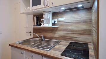 Una cocina compacta con microondas, cafetera y placa de inducción.