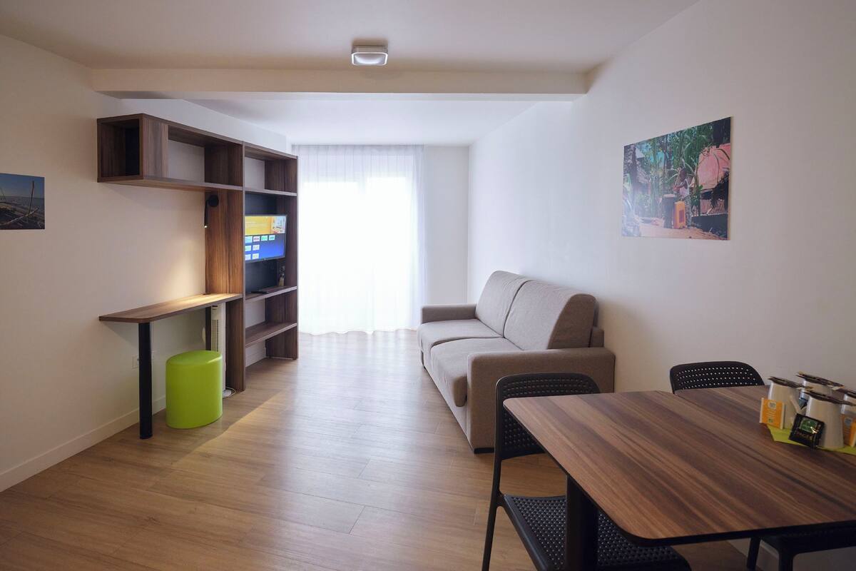 Un salon moderne avec un canapé, une table à manger et un téléviseur posé sur une étagère en bois.