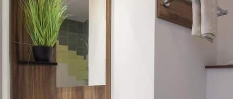 A modern bathroom with a white sink, dark cabinets, a mirror with a wooden frame, a potted plant, and a towel rack.