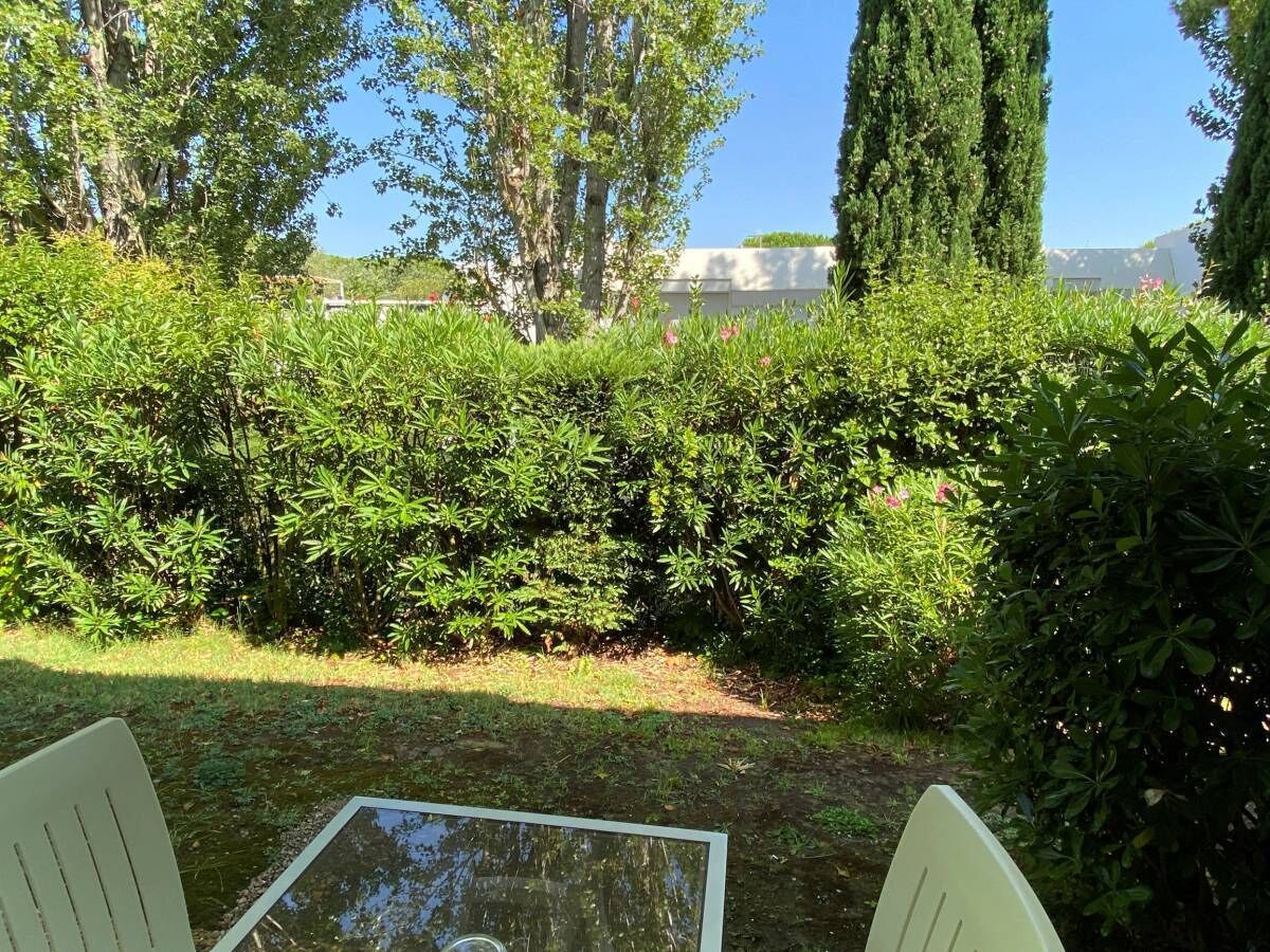 Un jardin avec une table et des chaises en verre, entouré d’une végétation luxuriante et de grands arbres.