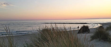 A beach scene with sand dunes and a person walking along the shore.