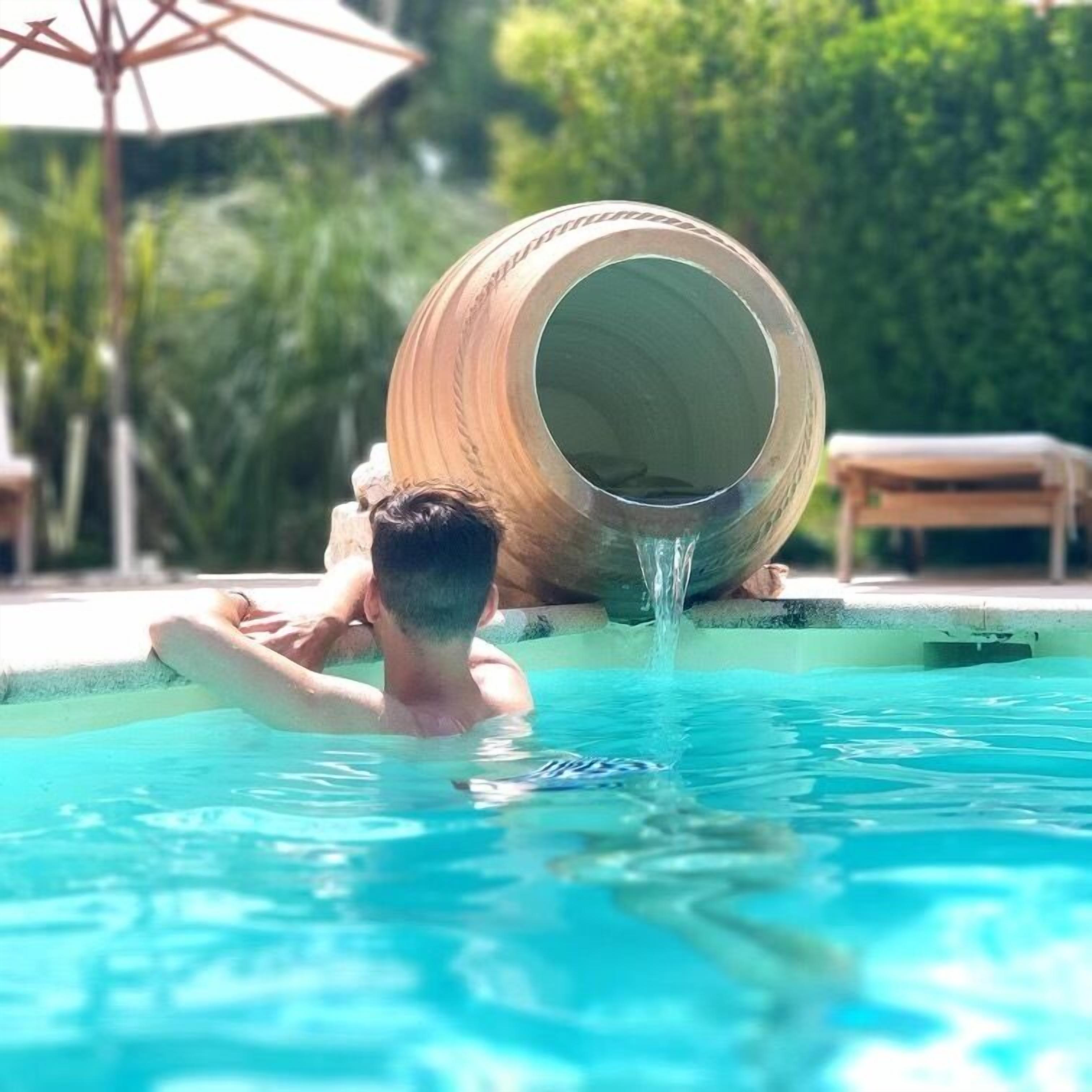 Une personne se détend dans une piscine, près d’un grand tonneau en bois.