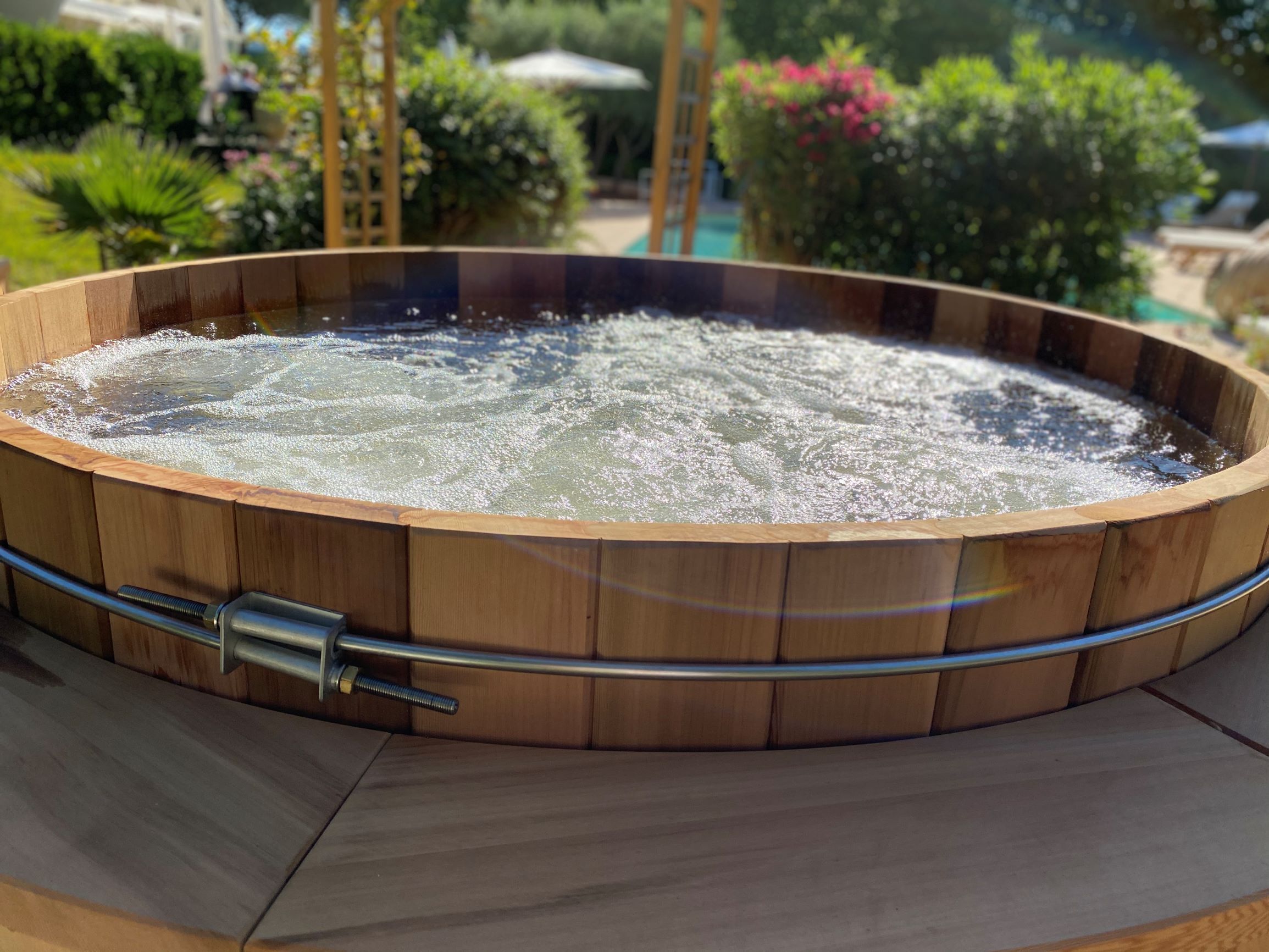 A hot tub with a wooden frame and a metal faucet, surrounded by a tiled patio.
