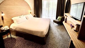Et hotelværelse med en stor seng, et skrivebord med lampe, et fjernsyn og udsigt til det fri.