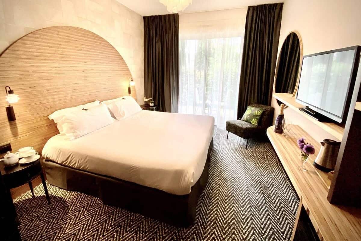 Une chambre d’hôtel avec un grand lit, un bureau avec une lampe, une télévision et une vue sur l’extérieur.