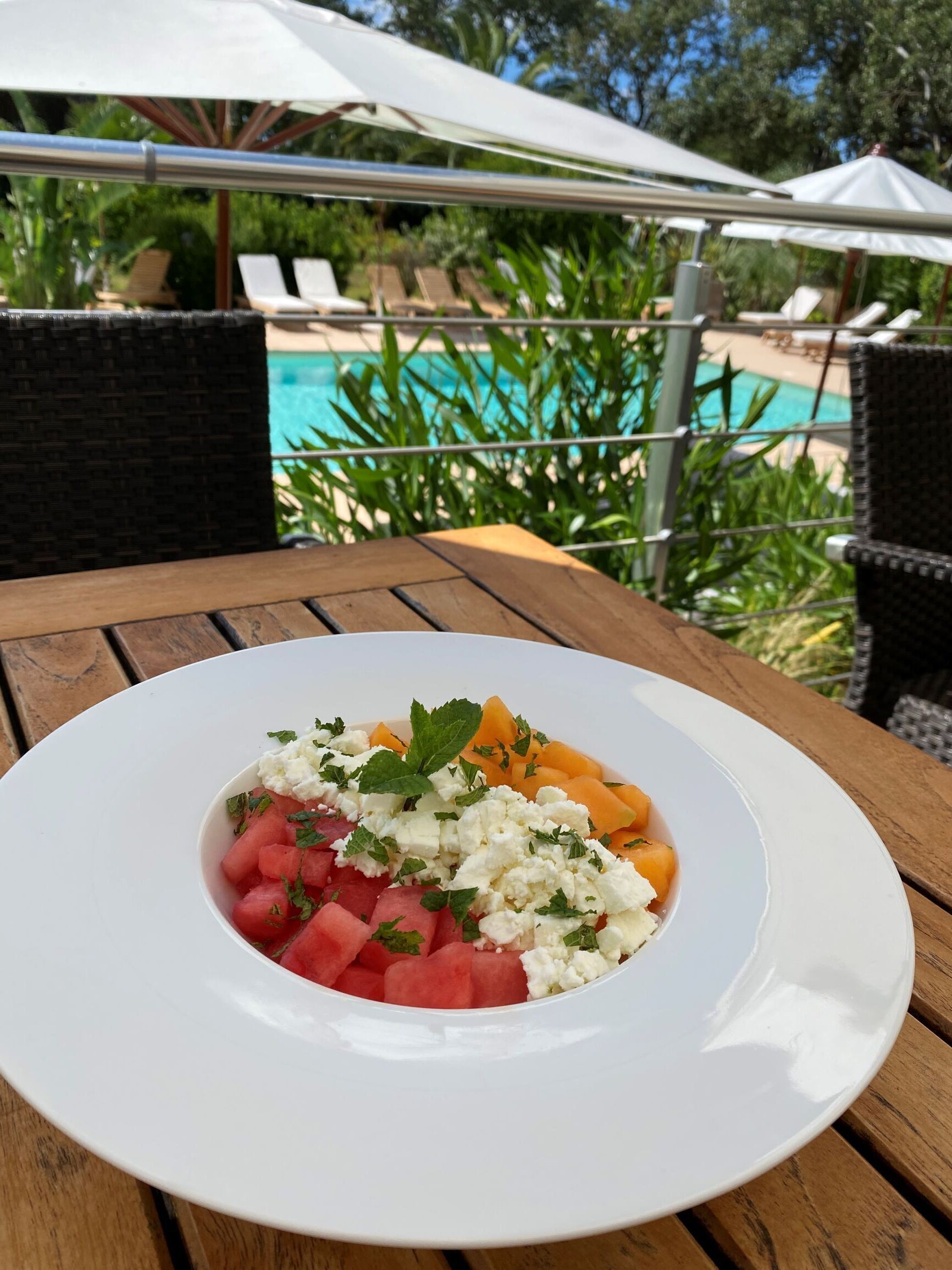 Une assiette blanche contenant de la pastèque, du fromage feta et de la menthe, posée sur une table en bois.