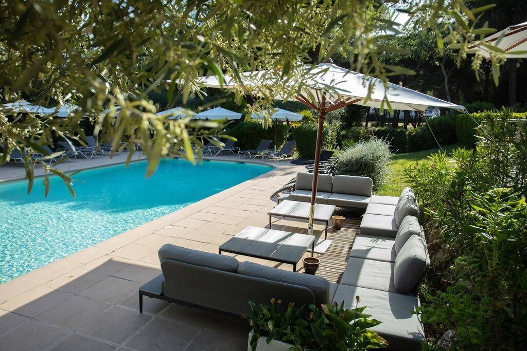 A poolside area with lounge chairs and umbrellas, surrounded by greenery.