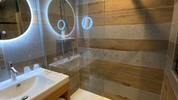 Un baño moderno con ducha de vidrio, tocador de madera y un espejo grande con luminarias circulares.