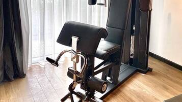 Een sportschool thuis met een hometrainer, een bankdrukrek en een kabeltoestel.