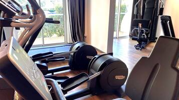 Un gimnasio con equipamiento cardiovascular, máquinas de pesas y un ventanal con vistas a zonas verdes.