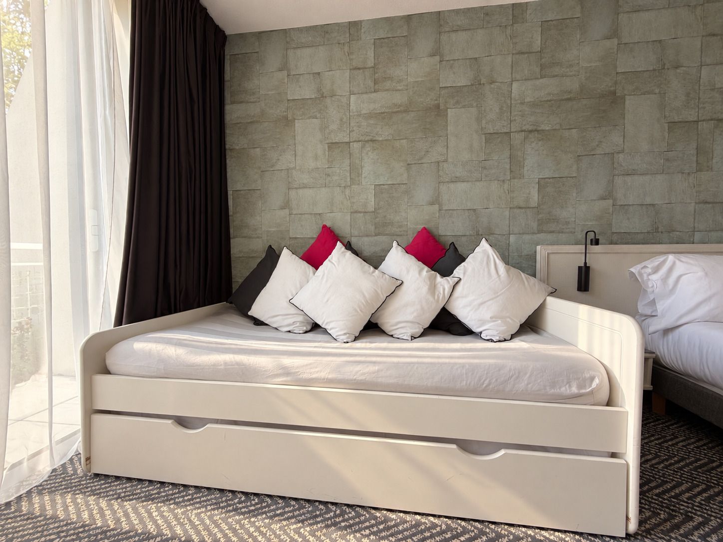 Un lit avec une tête de lit adossée à un mur texturé, une table de chevet et un tapis à motifs.