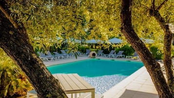 A poolside area with lounge chairs and a table, surrounded by trees.