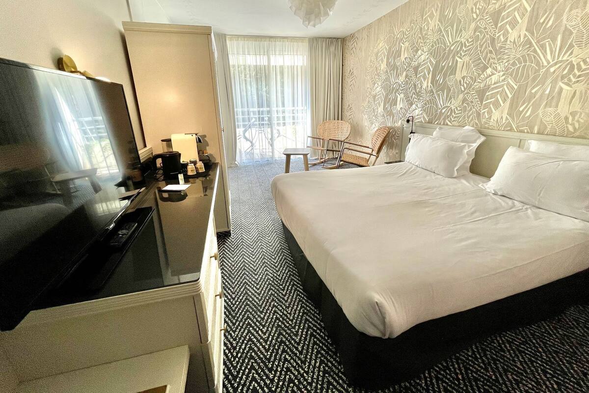 Une chambre d’hôtel avec un grand lit, une télévision, un bureau avec une machine à café et une chaise.