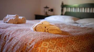 A bed with rolled towels and a patterned blanket.