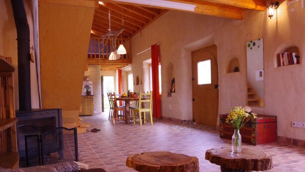 A cozy, rustic interior with wooden beams, a fireplace, a dining area, and a staircase leading to an upper level.