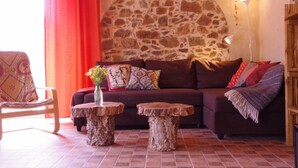 A cozy living room with a stone wall, a brown sofa, two wooden side tables, and a red curtain.
