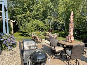 Eine Terrrasse im Freien mit Grill, Sitzgelegenheit und Garten im Hintergrund.