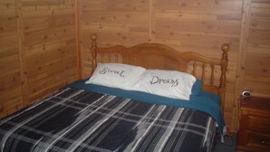Una stanza con rivestimenti in legno, un letto con copriletto a quadri e due cuscini con scritte.