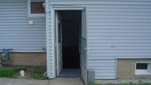 Un edificio residenziale con una porta aperta su un interno buio, una piccola finestra e un armadietto tecnico sul lato.