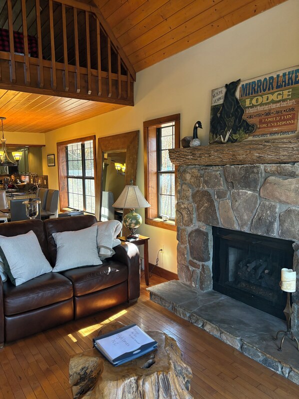 A cozy living room with a stone fireplace, a leather sofa, and a sign for Mirror Lake Lodge. - Red Top Treehouse Cabin in Mirror Lake and minutes to downtown-Dog Friendly! (Highlands)
