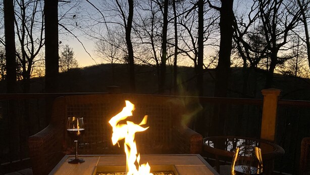 A fire feature with a glass table and chairs, surrounded by a wooden deck and trees. - Red Top Treehouse Cabin in Mirror Lake and minutes to downtown-Dog Friendly! (Highlands)