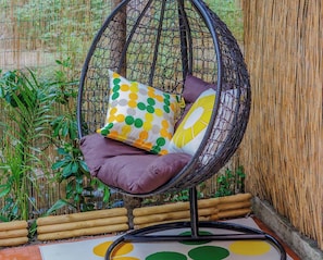 A hanging chair with cushions, positioned against a bamboo fence and a wooden floor with a circular pattern. - Sciacchetrà Ground Floor Apartment with AC and Patio (Monterosso al Mare)