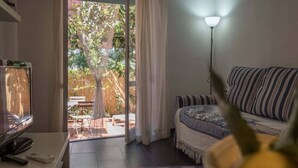 A room with a sofa, a lamp, a television, and a view of an outdoor patio with a table and chairs. - Sciacchetrà Ground Floor Apartment with AC (Monterosso al Mare)